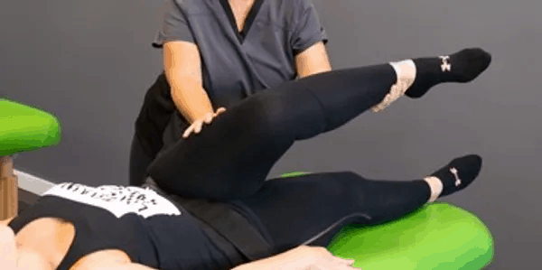 stretch therapist stretching a female client's leg while the client lies on a table