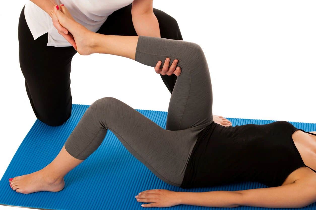 woman lying on yoga mat while her left leg is stretched by a stretch therapist