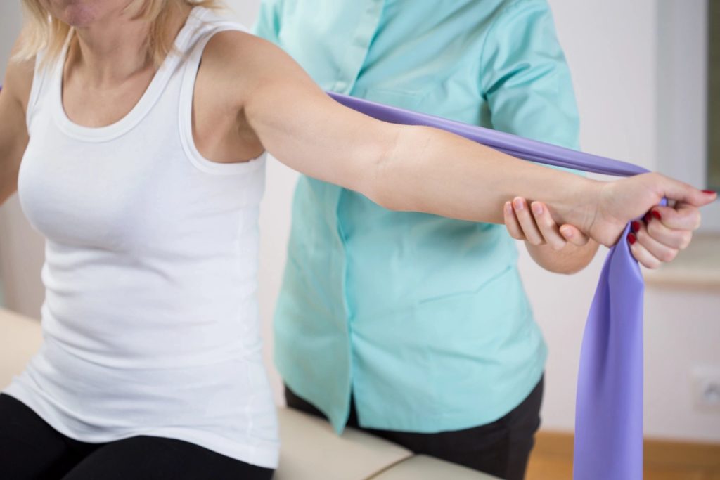 woman stretching using a large band with aid of therapist